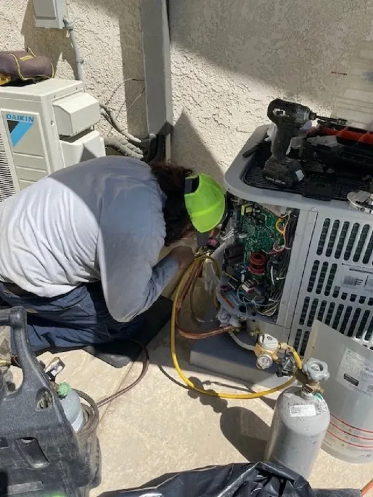 Technician servicing an air conditioning unit outdoors with tools and equipment nearby.